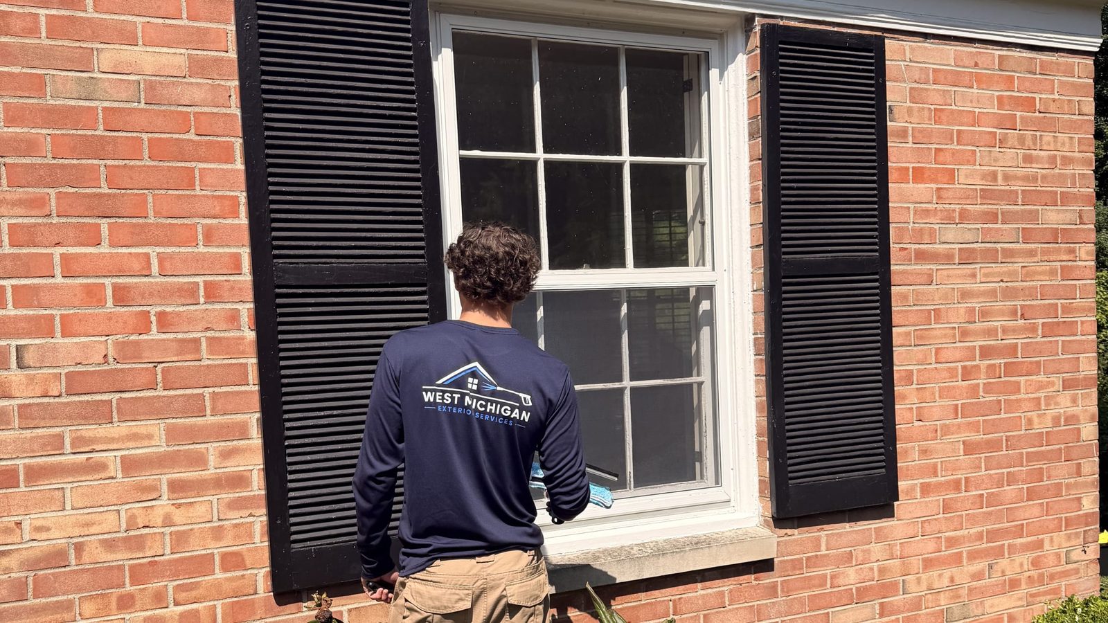 West Michigan Exterior Services technician cleaning the exterior windows of a brick home