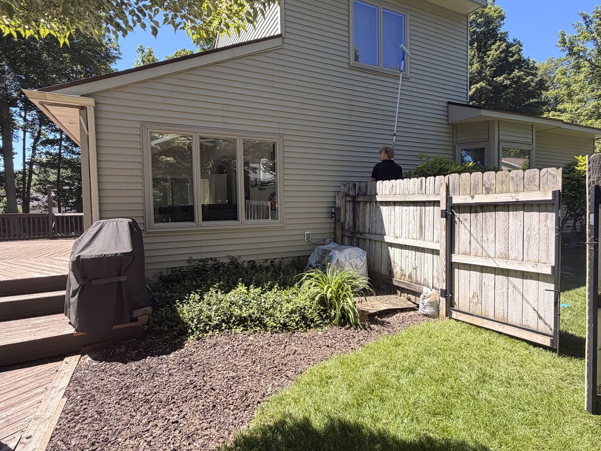 Technician soft washing house siding with an extension wand