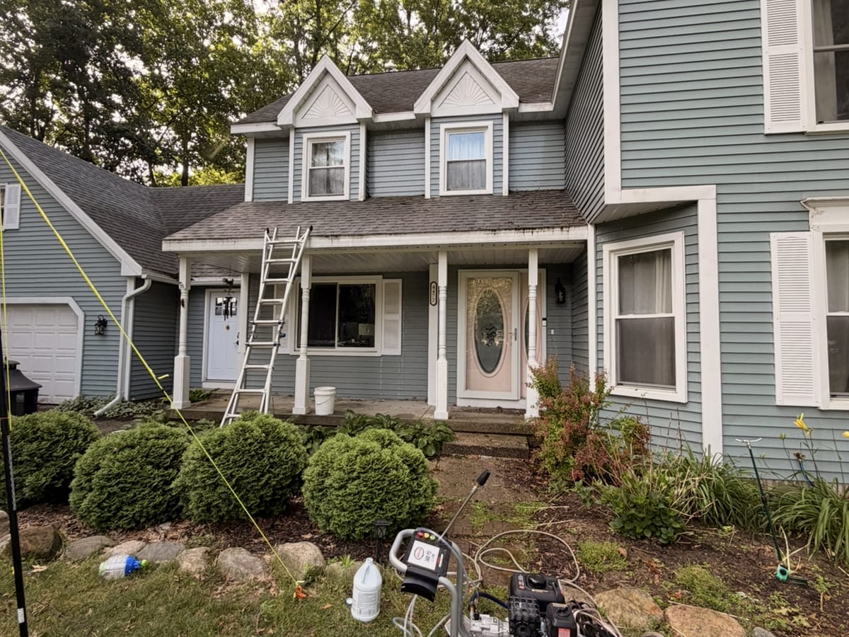 Two-story home with a ladder and pressure washing equipment set up before the exterior cleaning