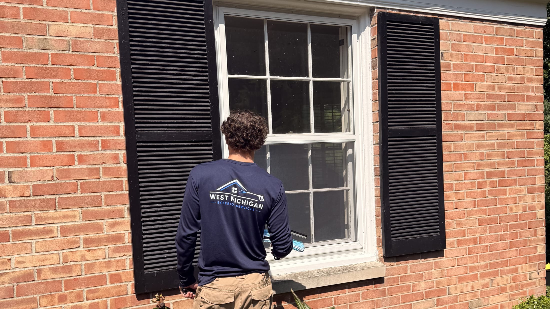 West Michigan Exterior Services technician cleaning the exterior windows of a brick home
